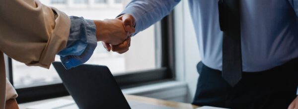 PPFD is a Proud Member of the Whitby Chamber of Commerce. News feature showing two professionals in business attire shaking hands over a desk with a laptop and documents, signifying a successful meeting or agreement.