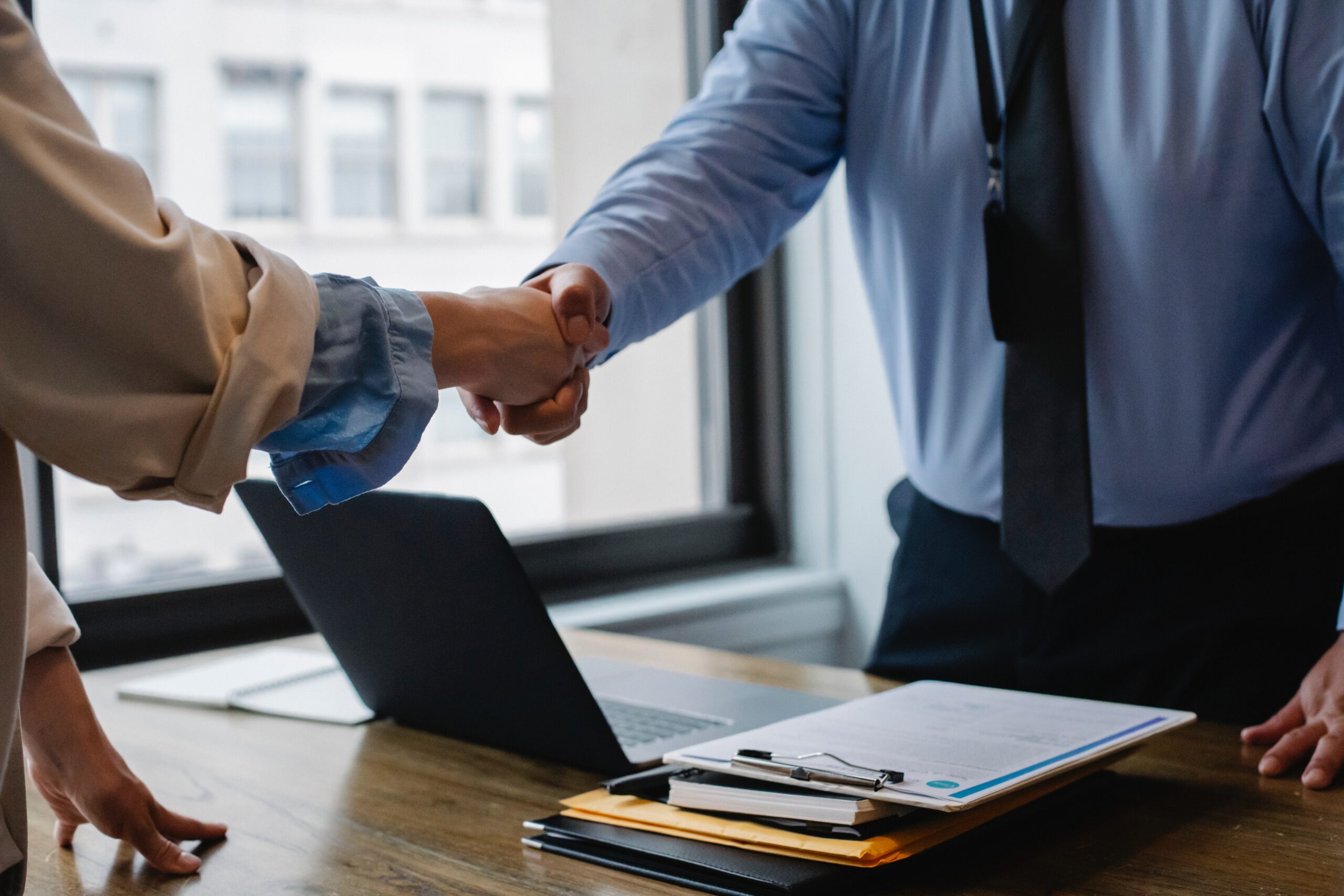 PPFD is a Proud Member of the Whitby Chamber of Commerce. News feature showing two professionals in business attire shaking hands over a desk with a laptop and documents, signifying a successful meeting or agreement.