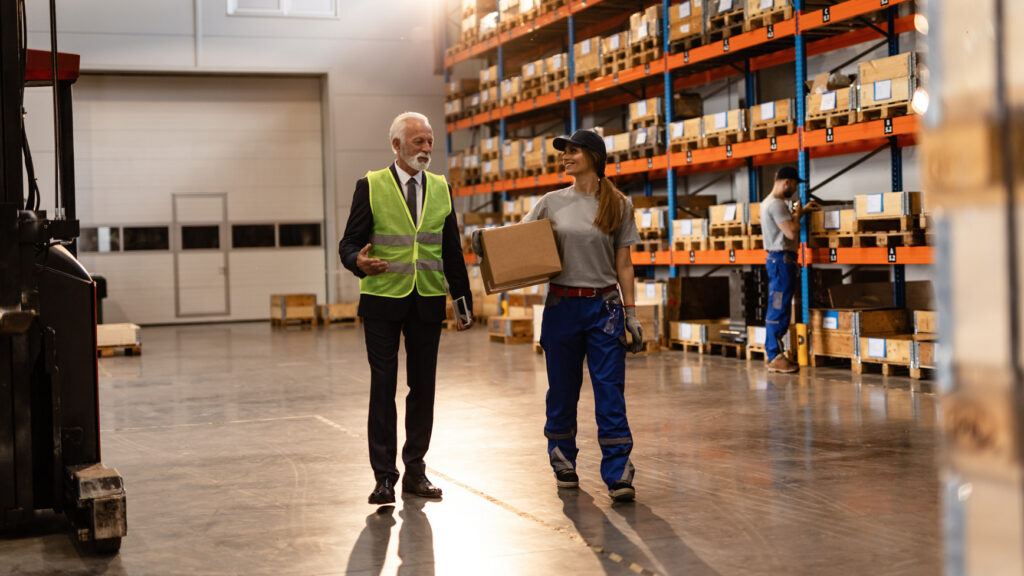 News update banner featuring a warehouse employee in blue coveralls and a supervisor with a safety vest conversing on the warehouse floor, with shelves of boxed inventory in the background. Celebrating 36 years.