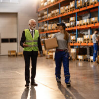 News update banner featuring a warehouse employee in blue coveralls and a supervisor with a safety vest conversing on the warehouse floor, with shelves of boxed inventory in the background. Celebrating 36 years.